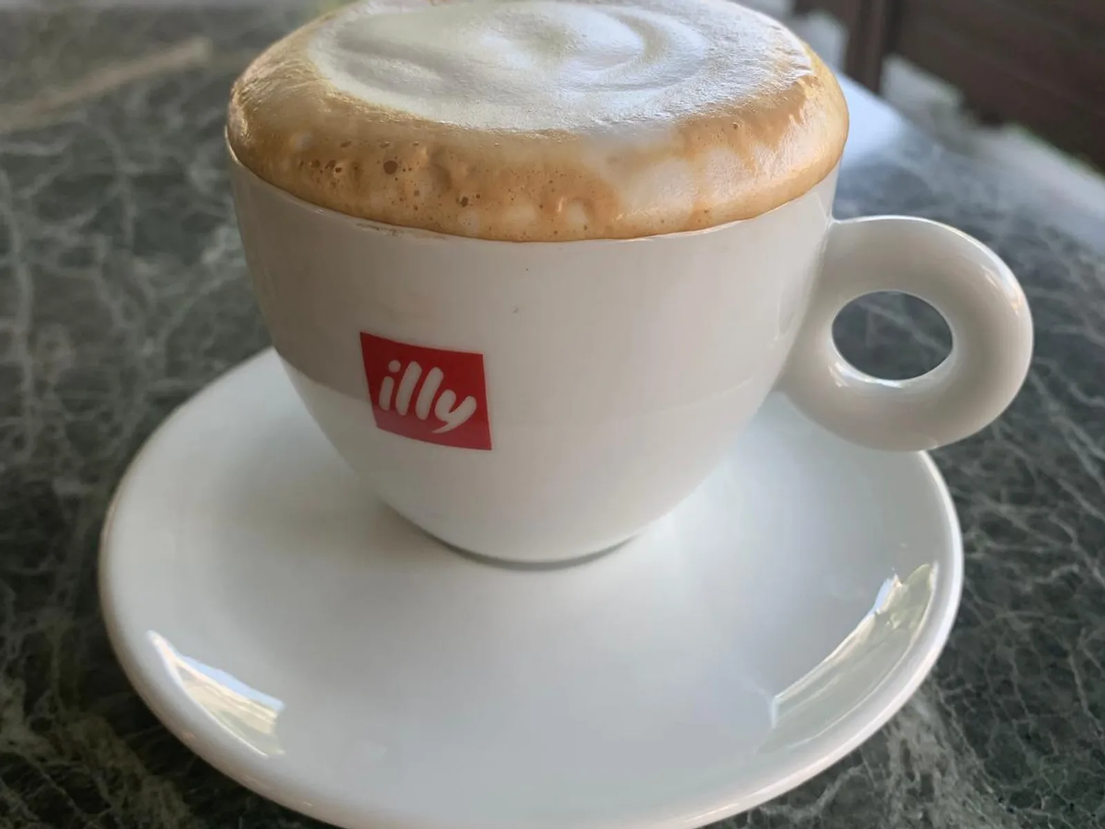 Yeşil mermer masada servis edilen illy cappuccino